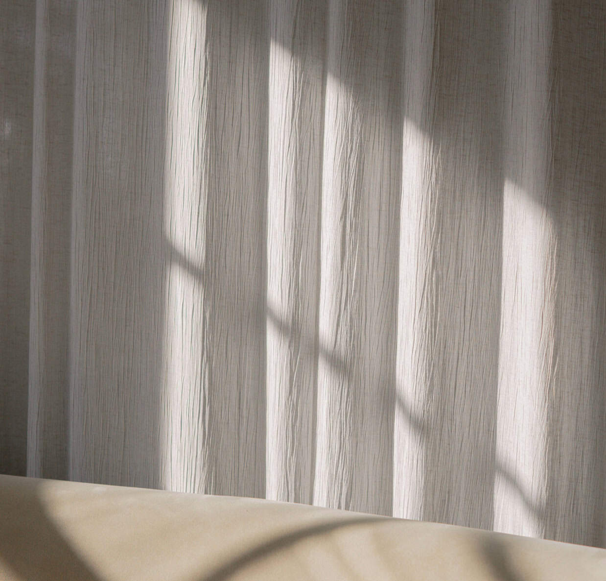 Sheer curtains casting soft shadows on a textured wall, creating a cozy and inviting atmosphere.
