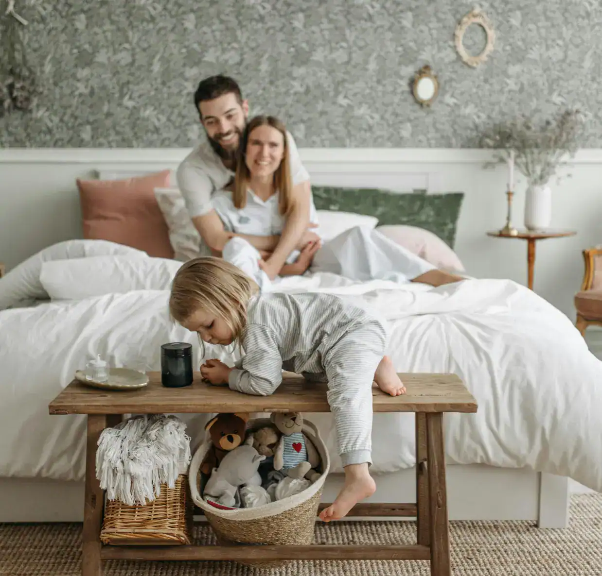 Family enjoying quality time in a cozy bedroom with a child playing on a wooden bench.