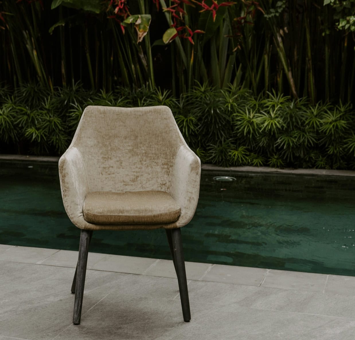Modern beige armchair by the poolside with lush greenery background.